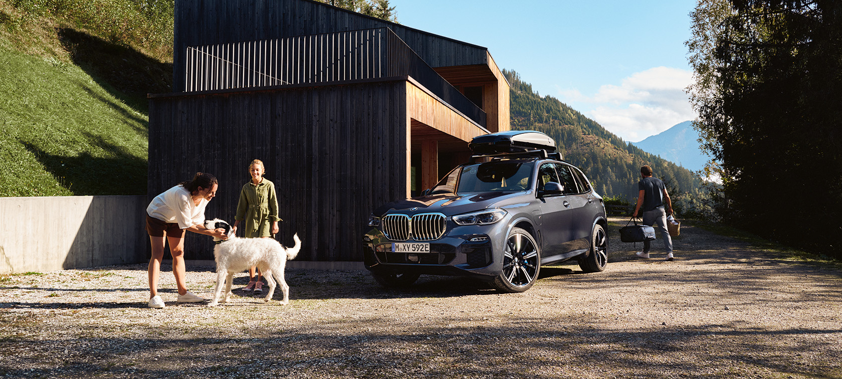 Familie med hund foran en BMW, der parkerer foran et hus om sommeren.